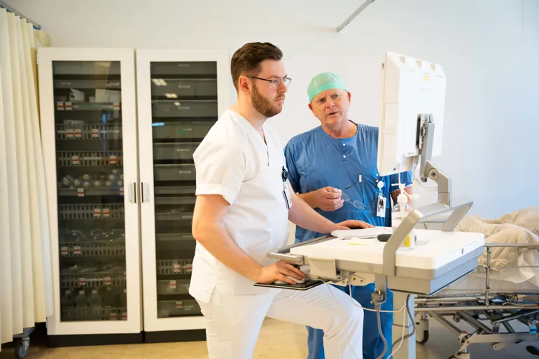 To menn kledd i hvitt og blått samtaler sammen inne på intenisv.