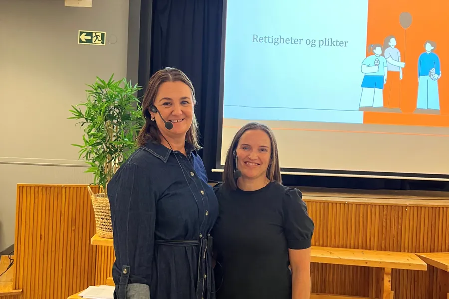 Et par kvinner som poserer for et bilde foran en stor skjerm